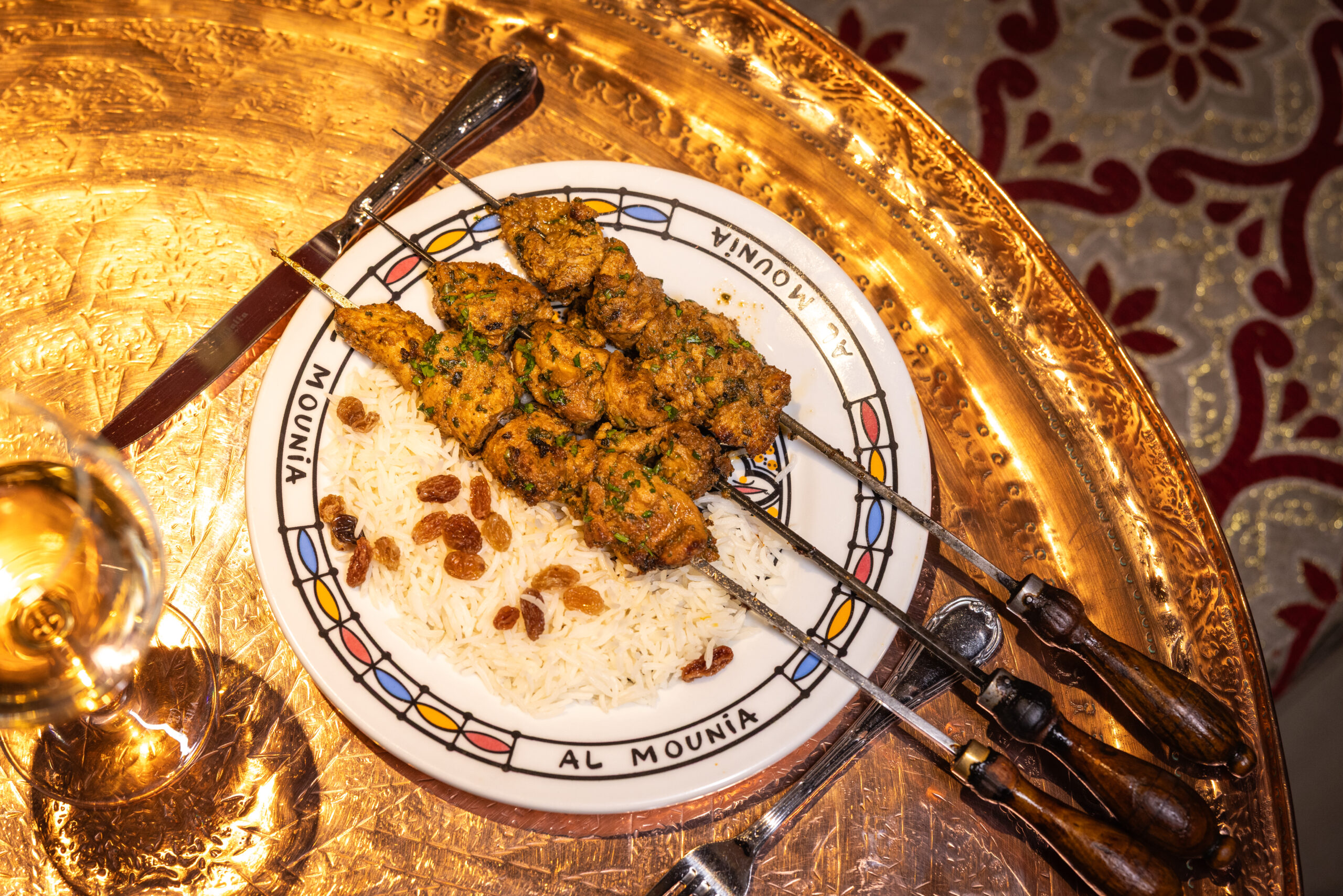 Brochetas de pollo especiadas con hierbas sobre arroz con pasas, bandeja dorada árabe - Al-Mounia Madrid