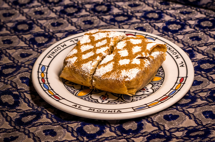 Pastela marroquí en hojaldre warka con azúcar glas y canela en plato Al-Mounia - restaurante árabe Madrid