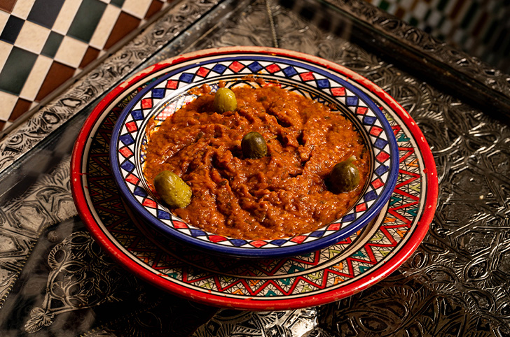 Zaalouk, puré de berenjena y tomate asado con aceitunas verdes en cuenco de cerámica marroquí pintada